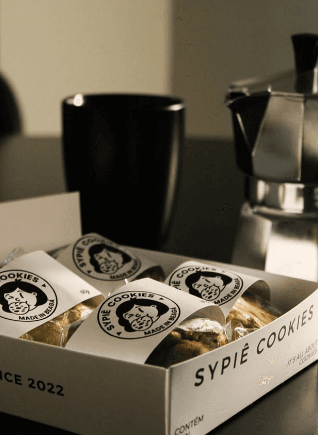 Caixa Sypiê aberta com quatro cookies ao lado de uma cafeteira