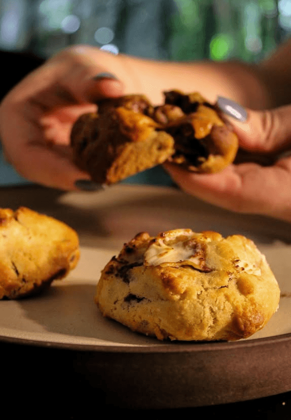 Mãos partindo um cookie quentinho com o recheio derretido